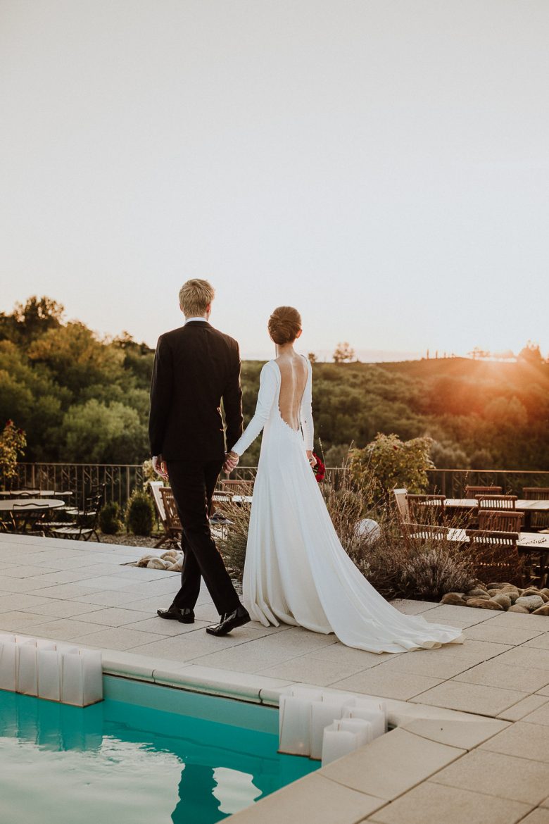 Freshly married couple walking by the pool of their wedding venue, taekn by thei wedding photographer in Italy